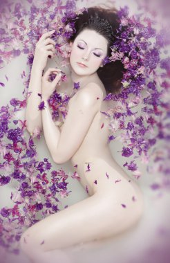Attractive naked girl enjoys a bath with milk and rose petals. Spa treatmen clipart