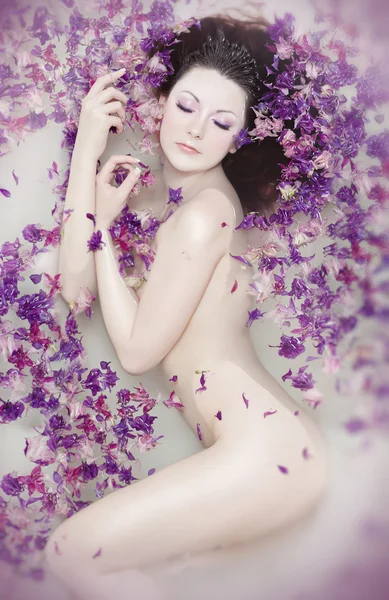 Chica desnuda atractiva disfruta de un baño con leche y pétalos de rosa. Tratantes de spa —  Fotos de Stock