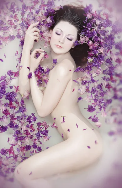 Menina nua atraente goza de um banho com leite e pétalas de rosa. Tratadores de spa Fotografia De Stock