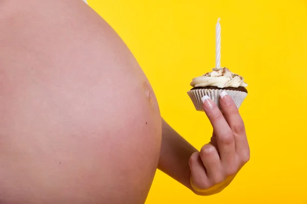 Вагітна жінка живіт і торт зі свічкою в руці — стокове фото
