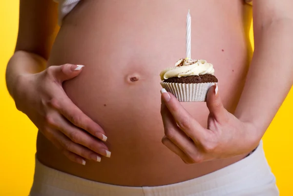 Pregnant woman belly and cake with candle in hand — Stock Photo, Image
