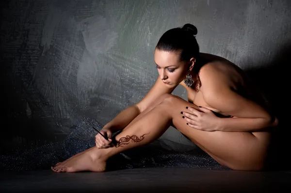 Mooie jonge vrouw toepassing van een tijdelijke tatoeage op haar been — Stockfoto