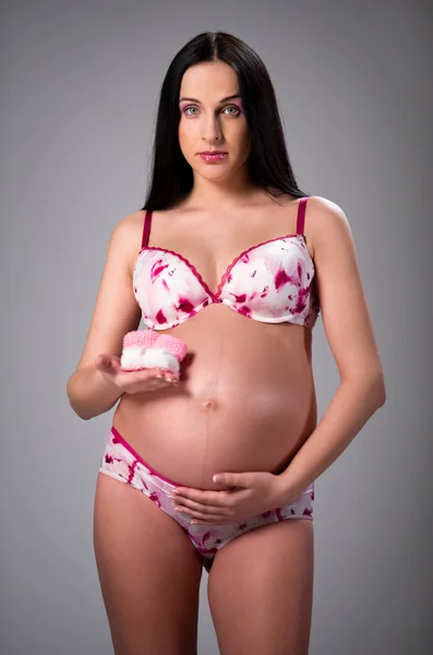 Linda mulher grávida segurando um par de botas de bebê rosa — Fotografia de Stock