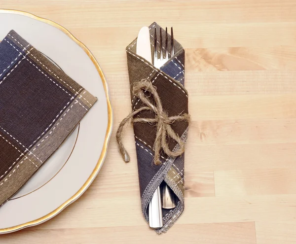 Coltello e forchetta in tovagliolo tessile su tavola di legno — Foto Stock