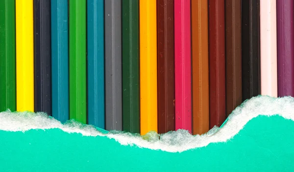 Green torn paper over color pencils — Stock Photo, Image