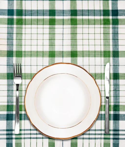 White plate on green checkered tablecloth with knife and fork — Stock Photo, Image