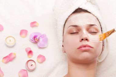 Applying of soothing mask, young woman getting spa procedures. clipart