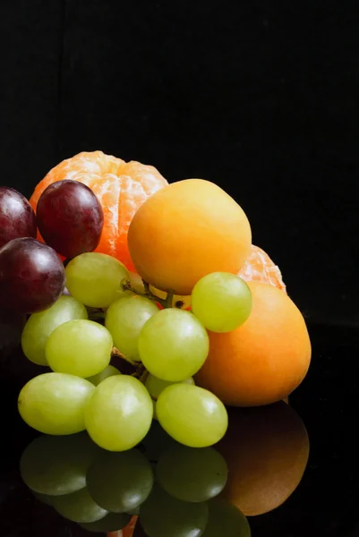 Mandarinen, Trauben, Federn und Pfirsiche vor schwarzem Hintergrund Stockfoto