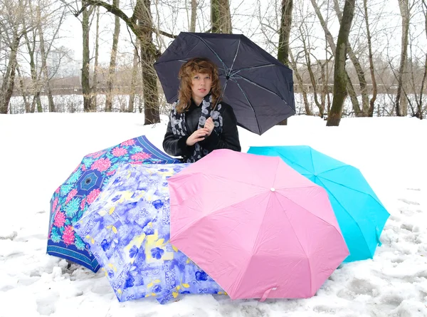 Девушка в весенней одежде с зонтиками на снегу зимой — стоковое фото