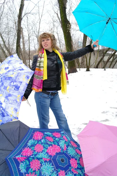 Девушка в весенней одежде с зонтиками на снегу зимой — стоковое фото