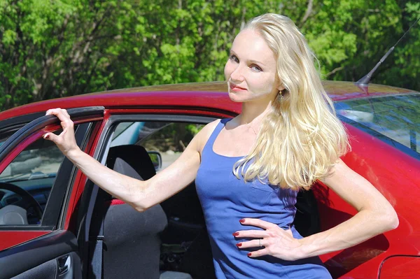 Девушка блондинка о красной машине летом — стоковое фото