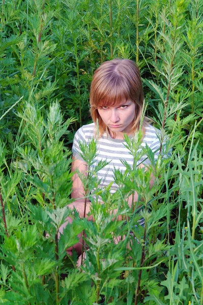 Offended by a sad girl sitting and hiding in the tall grass in the summer