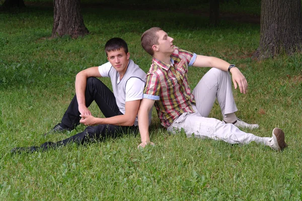 Zwei junge Männer sitzen auf dem Gras, Rücken an Rücken — Stockfoto