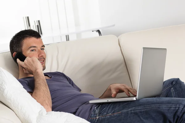 Людина на дивані з комп'ютером і телефоном — стокове фото