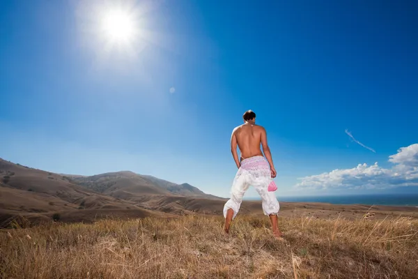 Glamour young man standing back in white skirt in mountains — Stock Photo, Image