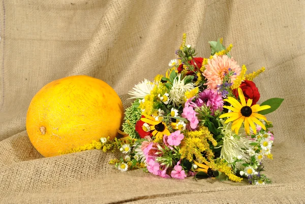 The orange melon and autumn flowers against rough stuff — Stock Photo, Image