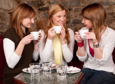 Three beautiful young students waiting drinking coffee and havi clipart