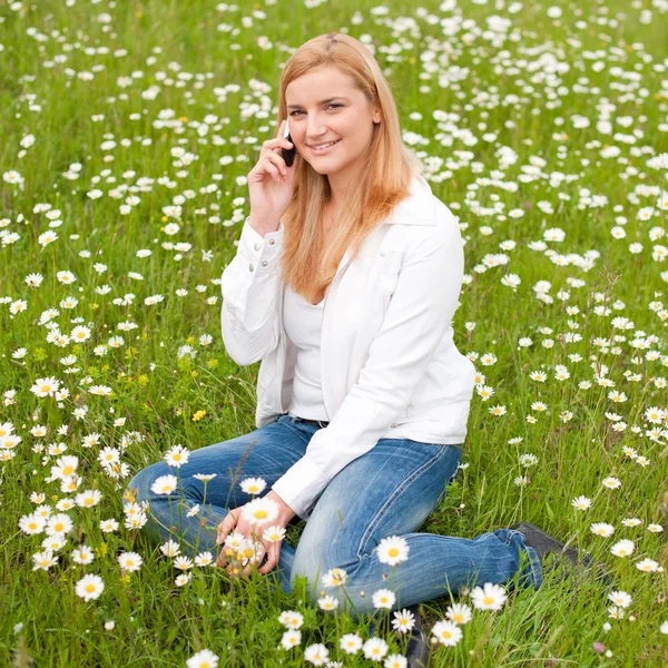 Krásná mladá žena, sedící na travnaté hřiště v parku a mluvíš — Stock fotografie