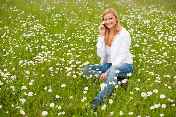 Hermosa joven sentada en un campo de hierba en el parque y hablando — Foto de Stock