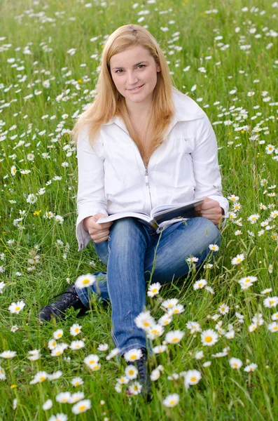 Beautiful young woman reading a book outdoors on a grass field i — Stock Photo, Image