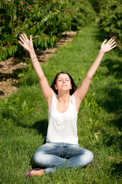 Linda joven sentada en el suelo con las manos arriba en la planta de cerezo — Foto de Stock