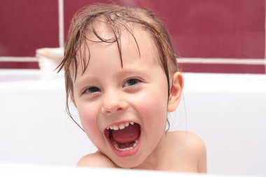 Cute three-year-old girl looking out of a bath and smiling clipart