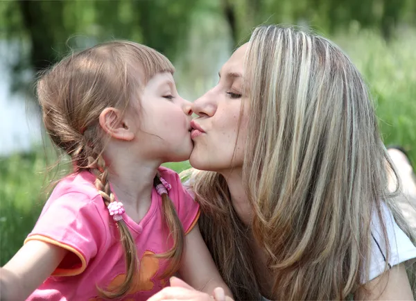 Lilla flickan kysser hennes mamma i en park — Stockfoto