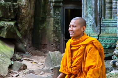 A monk sits on ruins of the Wat Ta Phrom temple at Angkor Wat in Cambodia clipart