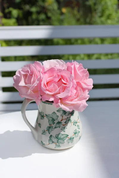 Рожеві садові троянди у вазі на білому столі — стокове фото
