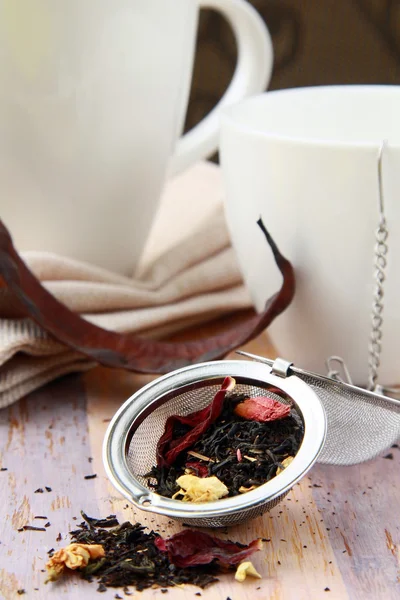 Teesieb mit einem duftenden schwarzen Tee und Tassen im Hintergrund — Stockfoto