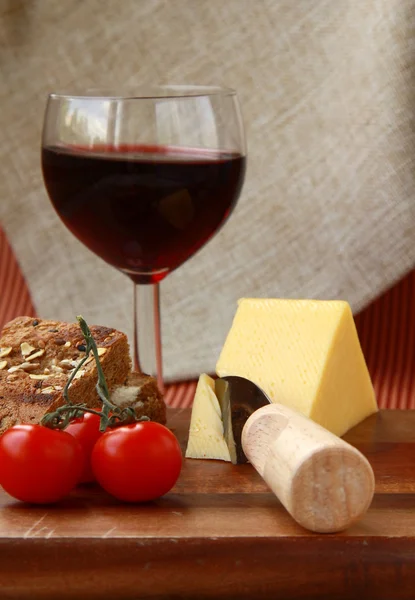 Prato de queijo com tomate cereja, pão e um copo de vinho — Fotografia de Stock