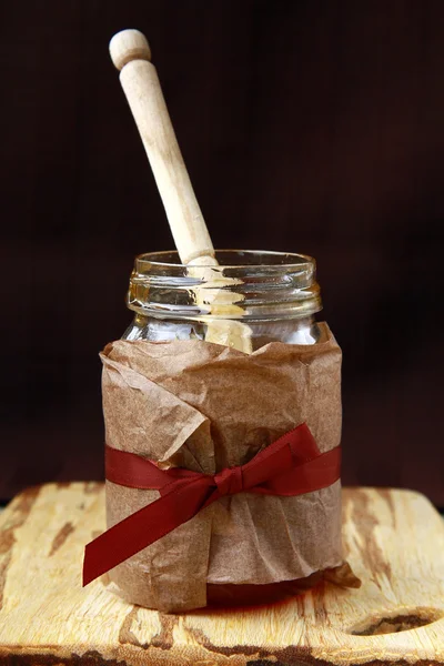 Jar with honey and wooden spoon for honey on a brown background — Stock Photo, Image