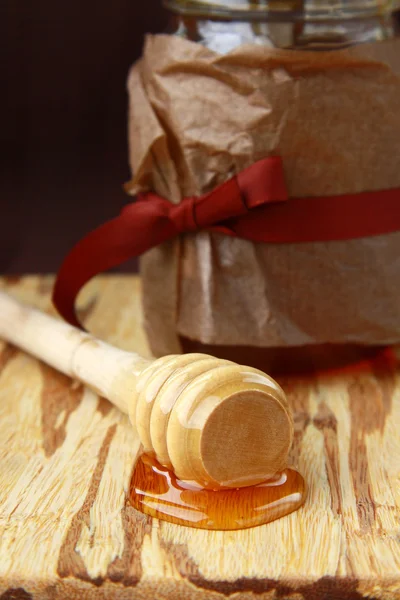 Банка с медом и деревянная ложка для меда на коричневом фоне — стоковое фото