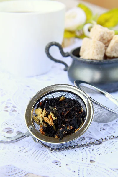 Colador de té con un té negro fragante y tazas en el fondo — Foto de Stock