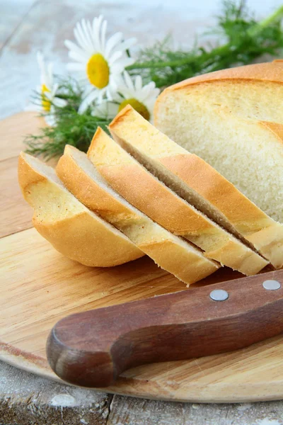 Świeży biały bochenek chleba z nożem i stokrotki, rustykalny — Zdjęcie stockowe