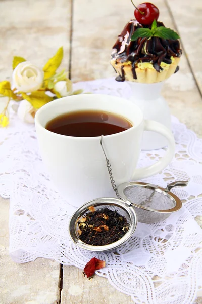 Colador de té con un té negro fragante y tazas en el fondo — Foto de Stock