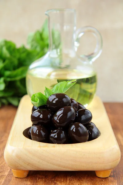 Olive nere e una bottiglia di olio su un supporto di legno — Foto Stock