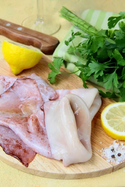 stock image Fresh raw squid on a kitchen board with herbs and lemon