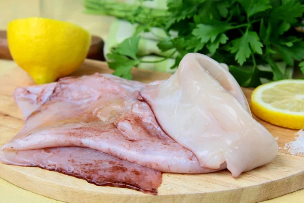 Свежий сырой кальмар на кухонной доске с травами и лимоном — стоковое фото