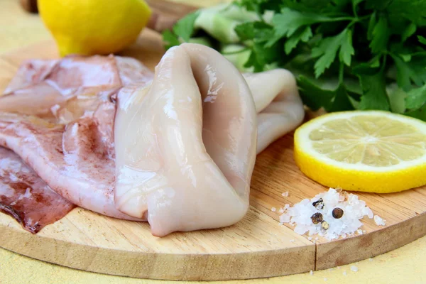 stock image Fresh raw squid on a kitchen board with herbs and lemon