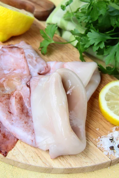 Calamari freschi e crudi su un tavolo da cucina con erbe aromatiche e limone — Foto Stock