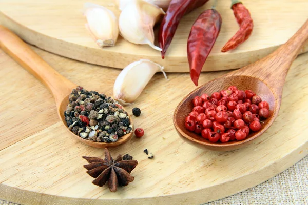 Spezie - pepe rosso e nero, peperoncino e aglio su uno sfondo di legno — Foto Stock