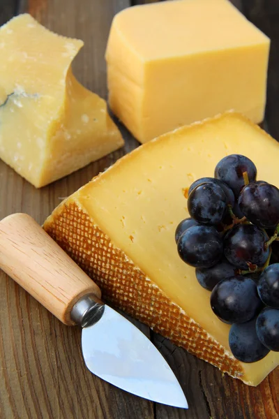 Prato de queijo com uvas em um fundo preto de madeira — Fotografia de Stock