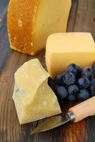 Prato de queijo com uvas em um fundo preto de madeira — Fotografia de Stock