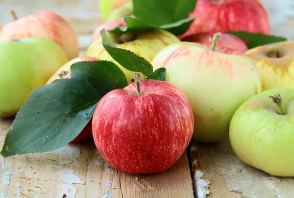 Κόκκινα, πράσινα και κίτρινα μήλα με φύλλα στο τραπέζι ξύλινο — Φωτογραφία Αρχείου