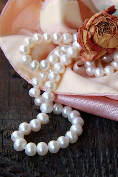 Bílé perly v růžovém sáčku s suchý růže — Stock fotografie