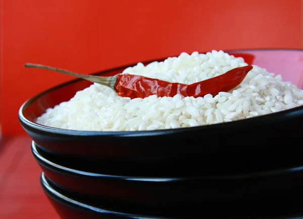 Arroz blanco en un tazón negro con chile sobre fondo rojo — Foto de Stock