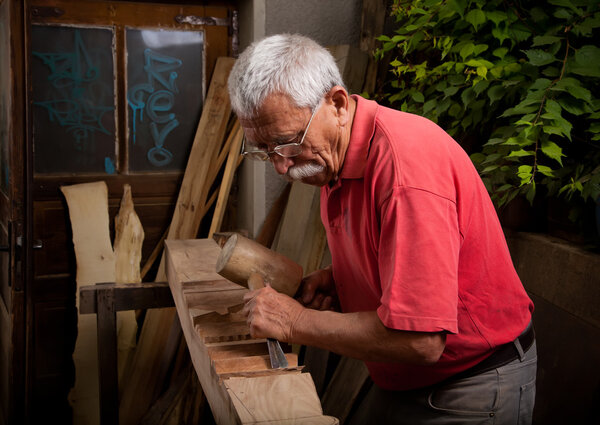 Old woodcarver working with mallet