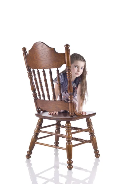 สาวน้อยนั่งบนเก้าอี้ไม้ที่สวยงามสลัก — ภาพถ่ายสต็อก