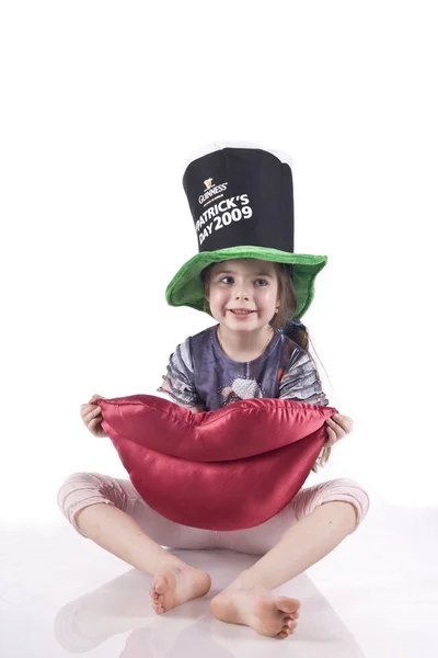 Liten flicka sitter på golvet i en svart hatt, hålla en leksak mjuka läppar — Stockfoto